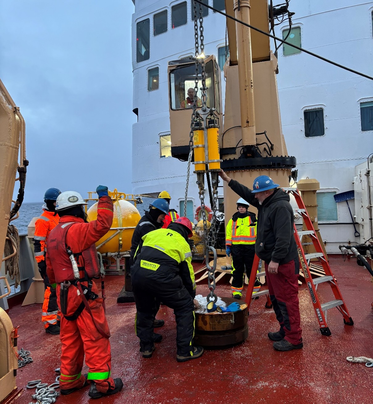 Photo 1: Jeff O’Brien, Jim Ryder, and Cory Beatty assembling Mooring D’s base (which includes an anchor, bottom pressure recorder, and acoustic releases) with the help of boatswain Rico Amamio and winchman Daryl Tobin. 