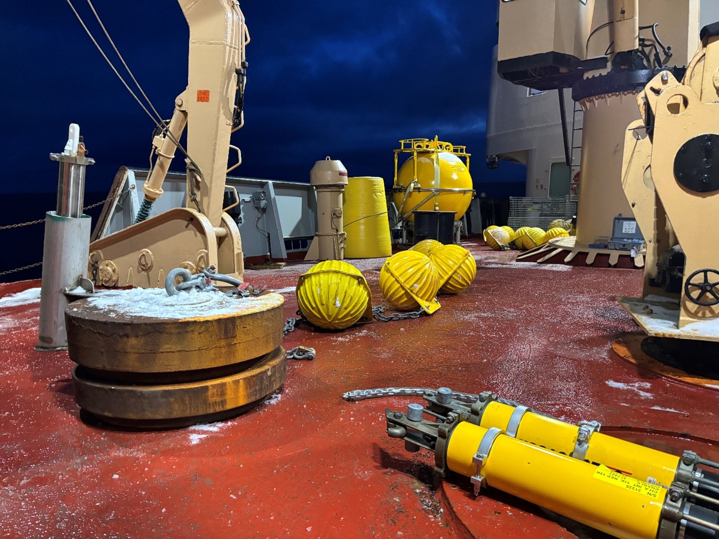 Photo 2: The components of Mooring A’s base (anchor, bottom pressure recorder, acoustic releases, glass balls) laid out prior to deployment. 