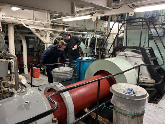 Picture17 Photo 5: Engine room assistant Kyle Brinson	(left) and second engineer Joshua Genter (right) examining one of the propeller shafts.