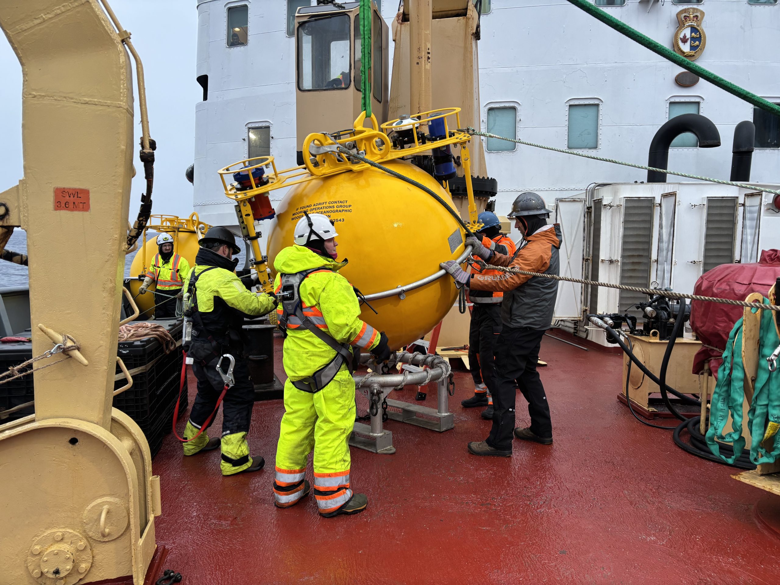 The WHOI team working with the deck crew to bring Mooring D’s top sphere on deck. Photo by Jennifer Kosty. 