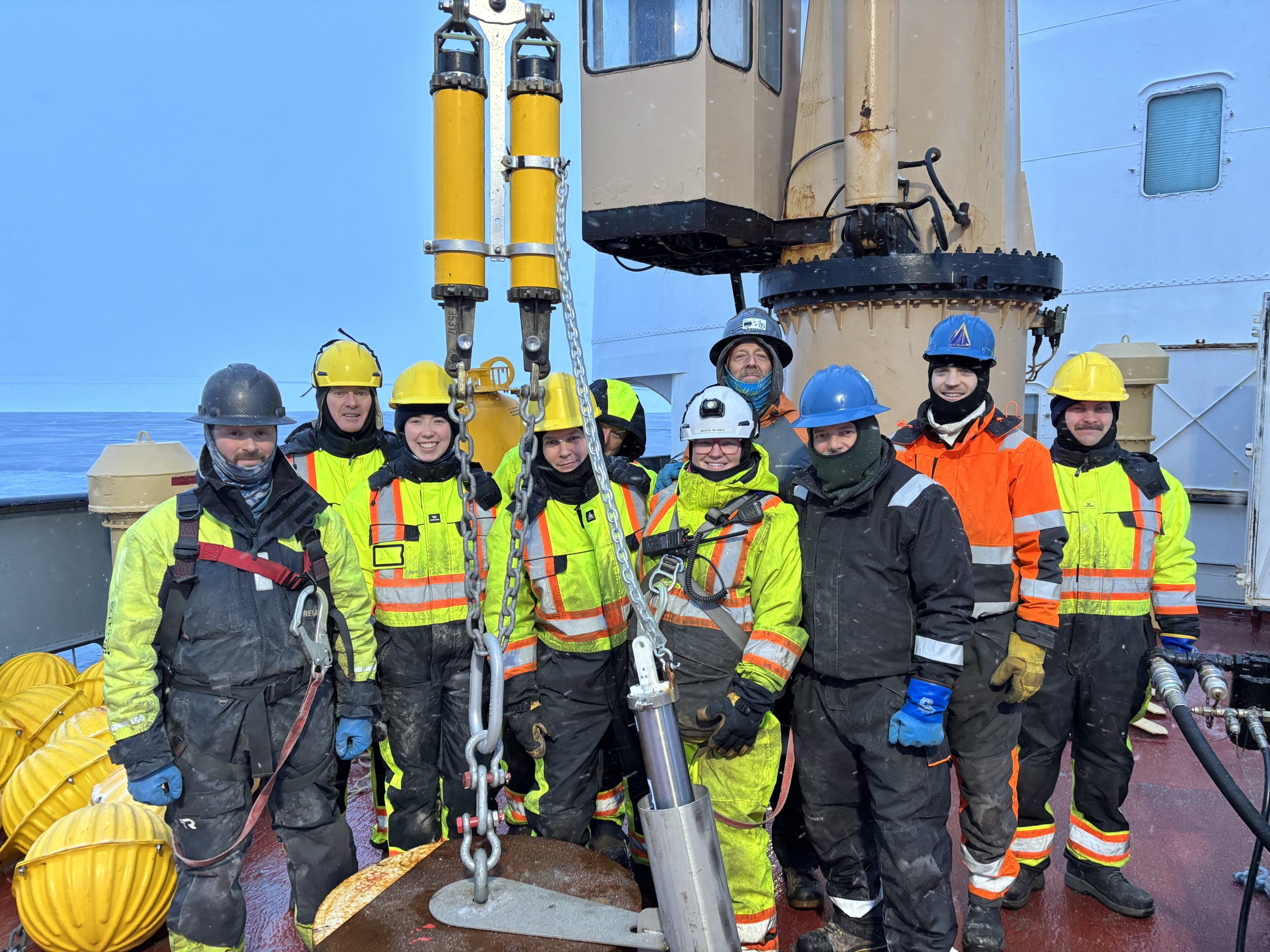 The WHOI team and deck crew posing with Mooring A’s anchor before its deployment. Photo by Jennifer Kosty. 