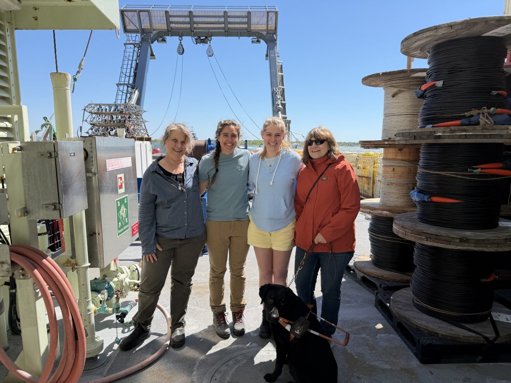 From left to right: Heather, Ali, Anna and Amy smile on the deck of the R/V Neil Armstrong on a clear sunny day. Bonnie sits in front of Amy and Anna facing the camera.