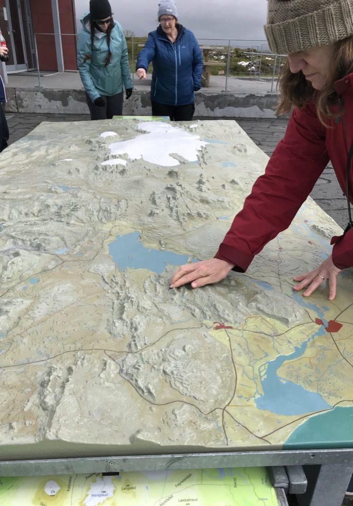 Photo of Amy Bower reaching across and examining a 3-D topographic map of the Iceland during a geological field trip.