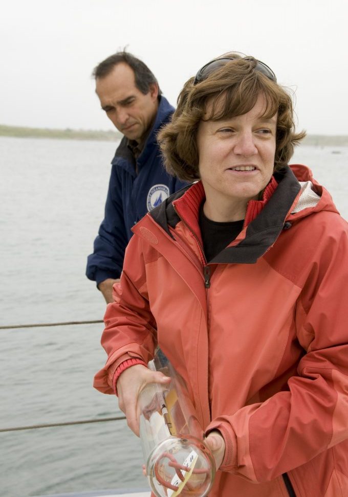 Photo of Amy Bower and Dave Fisichella standing on a ship’s deck while holding a long glass deep ocean drifter.