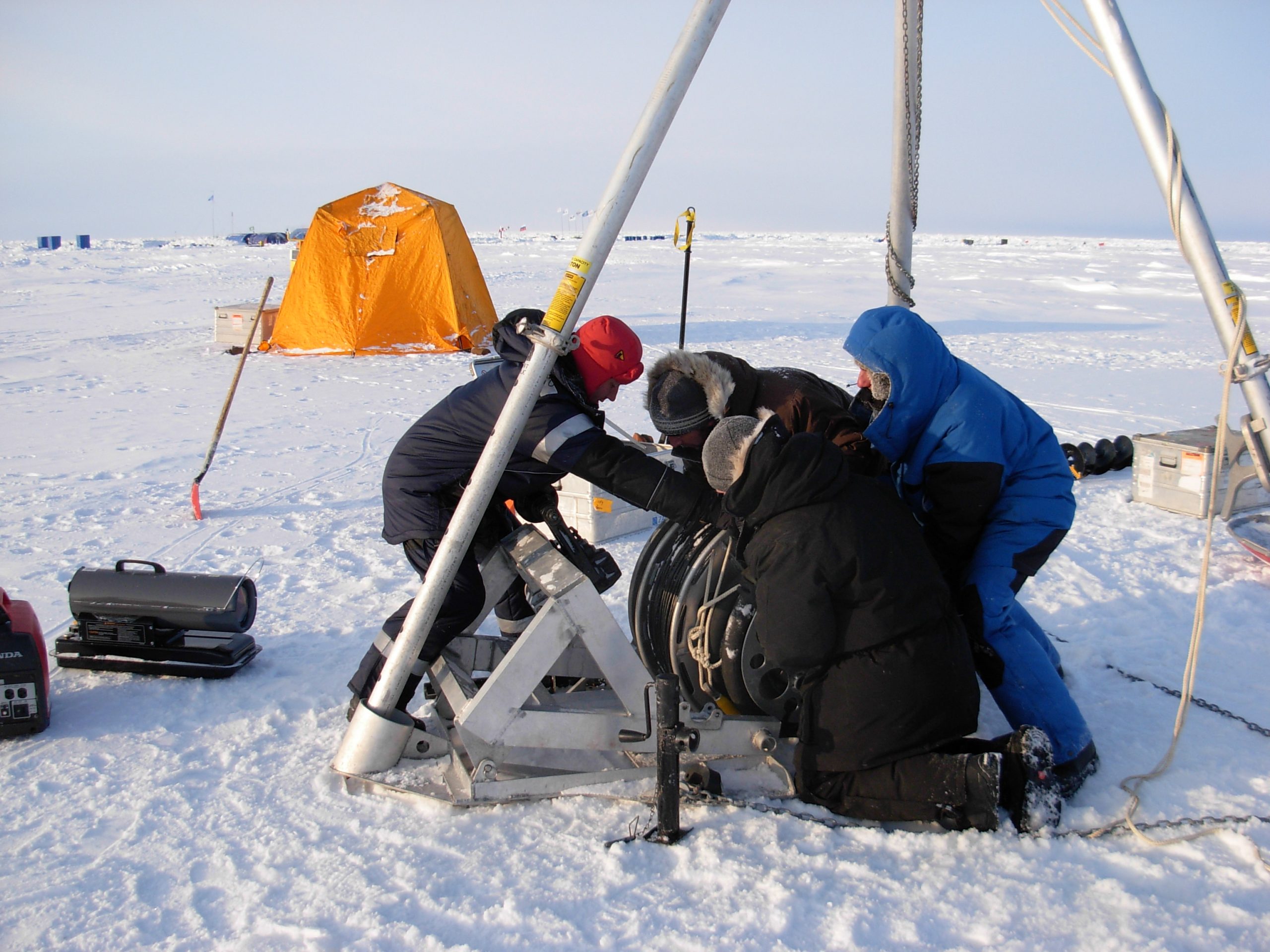 ITP wire being maneuvered onto deployment winch by Sergey Pisarev, Chris Basque, Jeff Pietro, and Denis Dausse.  Working tent and ice camp Barneo are in the background. (Photo by Rick Krishfield)