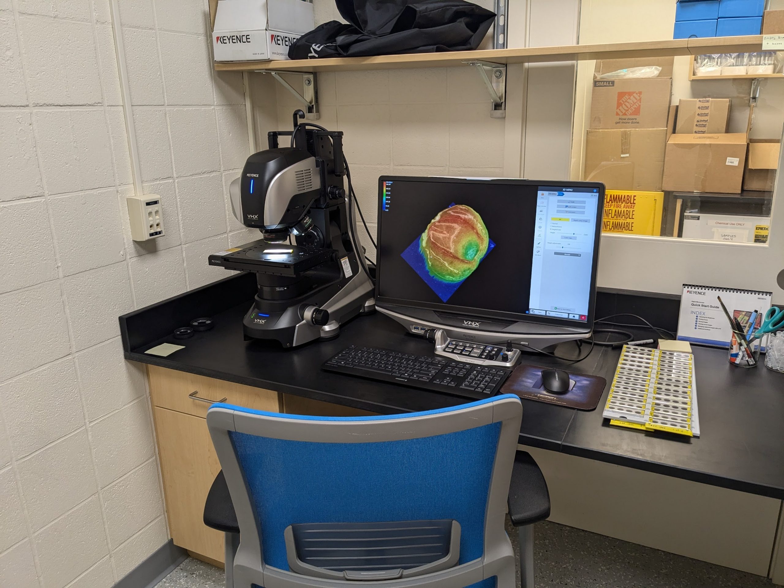 The Keyence VHX-7100 digital microscope setup sits on a seated-height desk. It is comprised of two parts: a microscope, which has a mechanized stage and head and is approximately 1 foot square and 1.5 feet tall, and a monitor, which displays the output that the microscope is observing. The monitor is displaying the three-dimensional surface plot of a shark dermal denticle imaged by the Keyence.