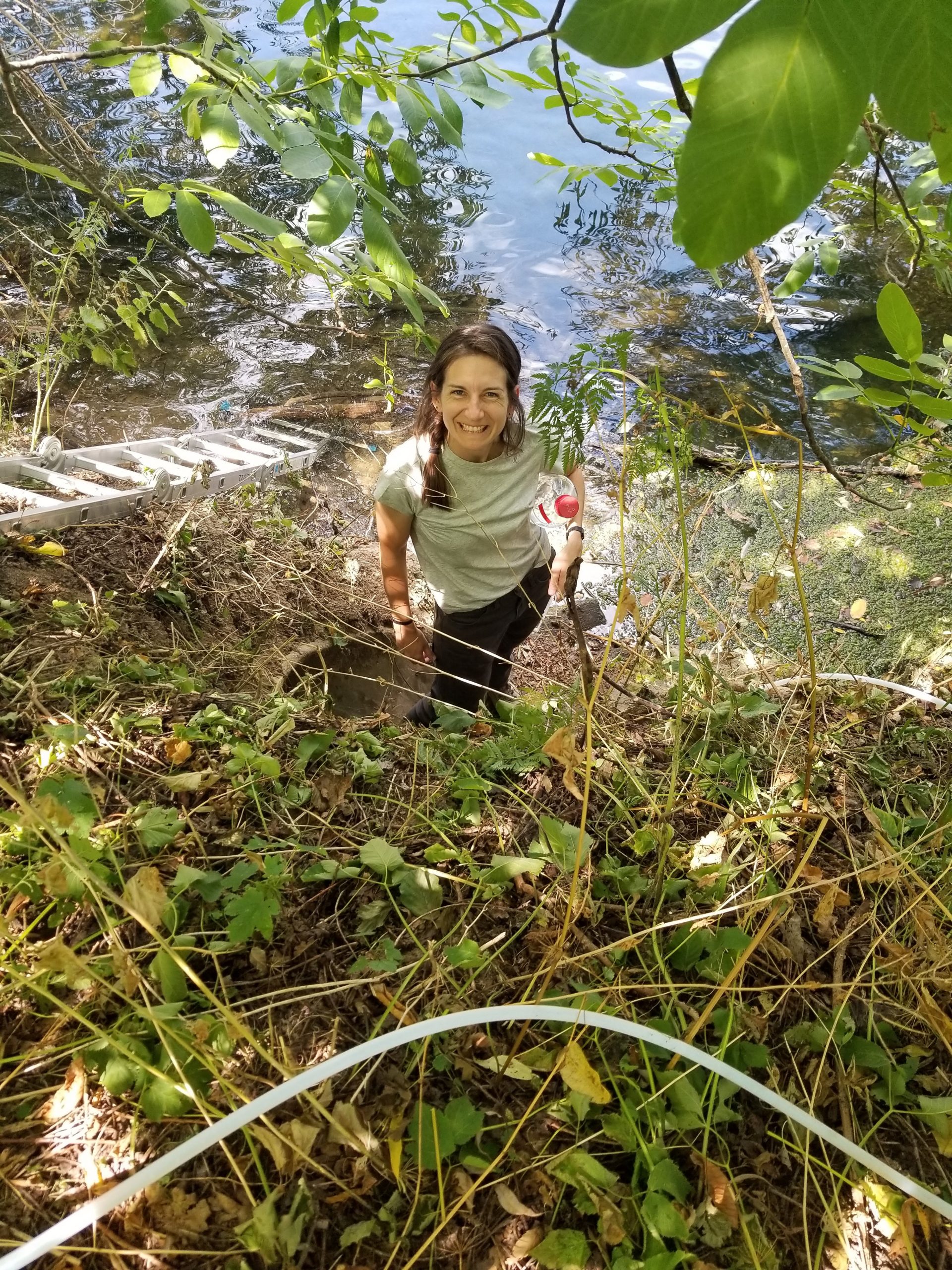 Lana Graves in the field, smiling and holding a water sample bottle.