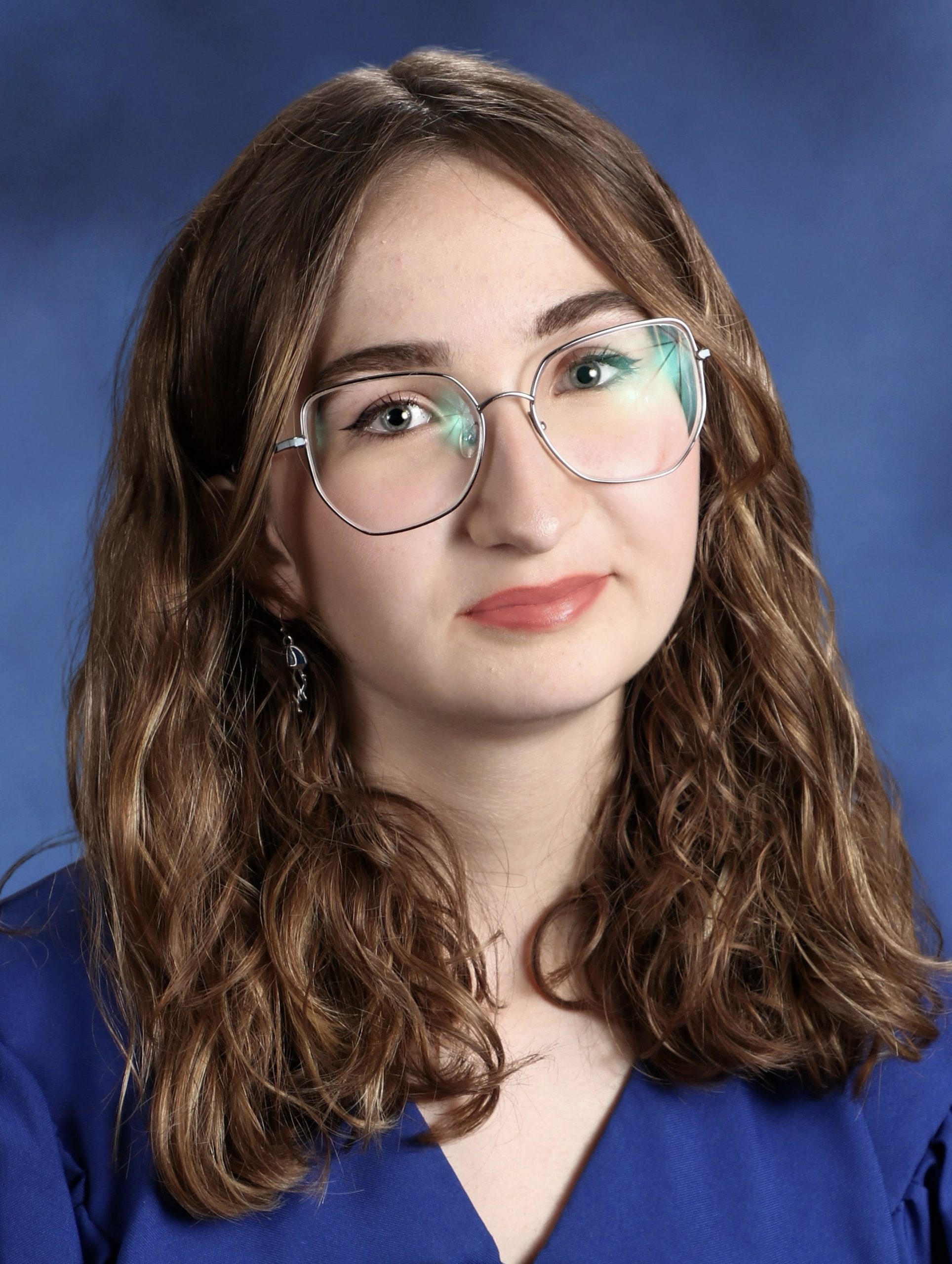 Headshot of Ella Friedman smiling in front of a blue backdrop, wearing a blue blouse and glasses.