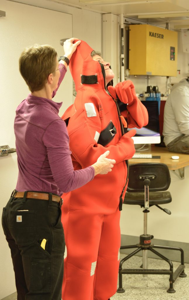 A safety briefing was the first activity aboard the R/V Neil Armstrong.  Dee Emrich dons a “Gumby” survival suit as instructed by Chief Mate Jen Hickey. 